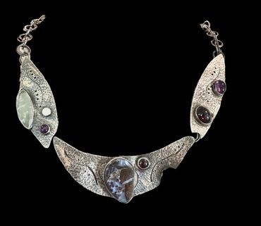 Artistic silver necklace with embedded stones and intricate textures.