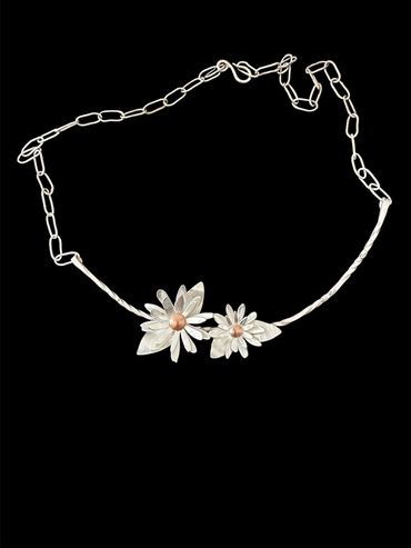 Silver chain necklace with two daisy flower pendants on a black background.