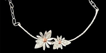 Silver necklace with two flower pendants on a black background.