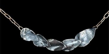 Silver leaf-shaped necklace on a black background.