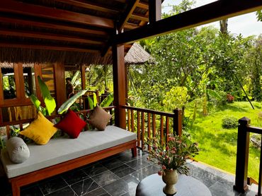 Cozy wooden porch with colorful cushions overlooking a lush green garden.