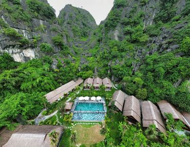 Resort nestled in lush green mountains with a central swimming pool and thatched-roof buildings.