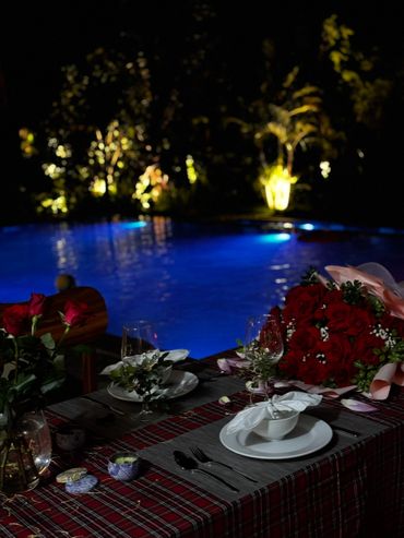 Romantic poolside dinner setup with red roses and soft lighting.