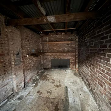 Empty, narrow room with exposed brick walls and wooden shelves.