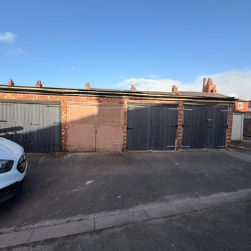 Row of brick garages with metal doors under a clear blue sky.