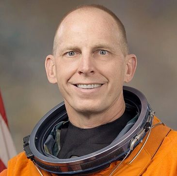 Astronaut in orange space suit smiling at the camera.