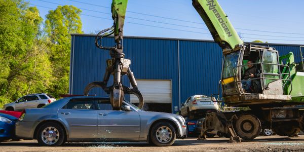 A crane lifting a silver car at a junkyard.