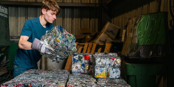 Worker handling compressed aluminum cans in recycling plant.