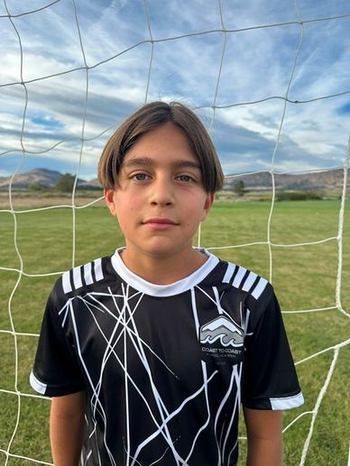 Boy in a soccer jersey in front of a goal net.