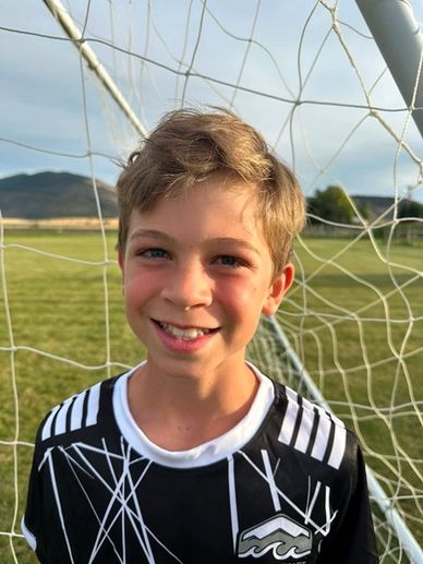 Smiling boy in soccer jersey by goal net.