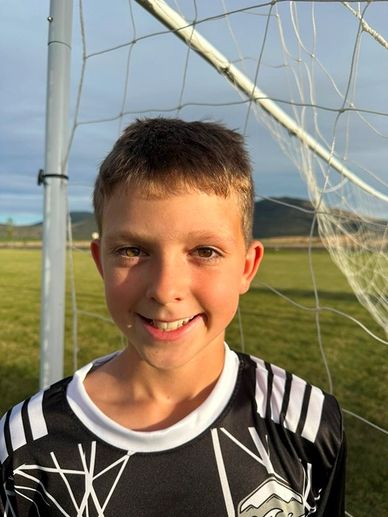 Smiling boy in soccer jersey by goal net.