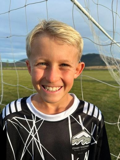 Smiling boy in soccer attire standing in front of a net.