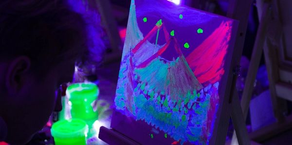 Person painting neon mountains under blacklight.