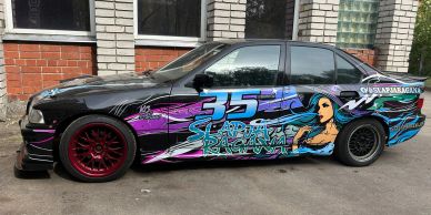 Black car with vibrant graffiti art and red rims.