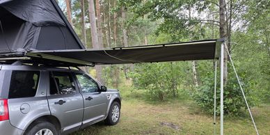 SUV with rooftop tent and extended awning in forest.