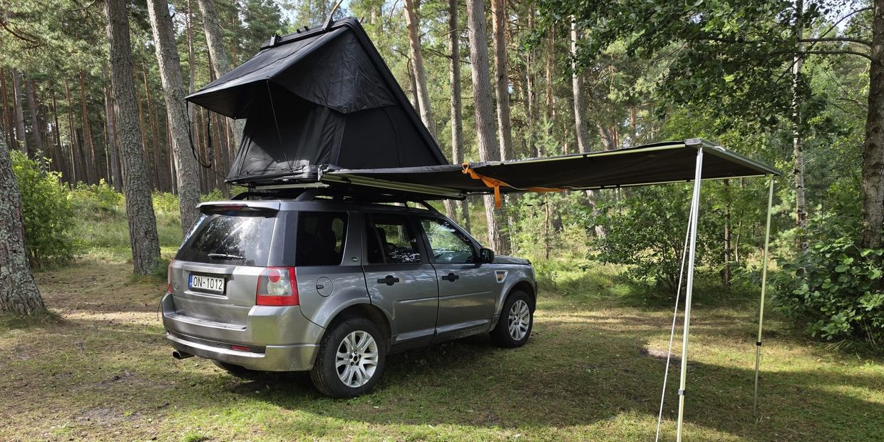 SUV with rooftop tent and extended awning in forest.