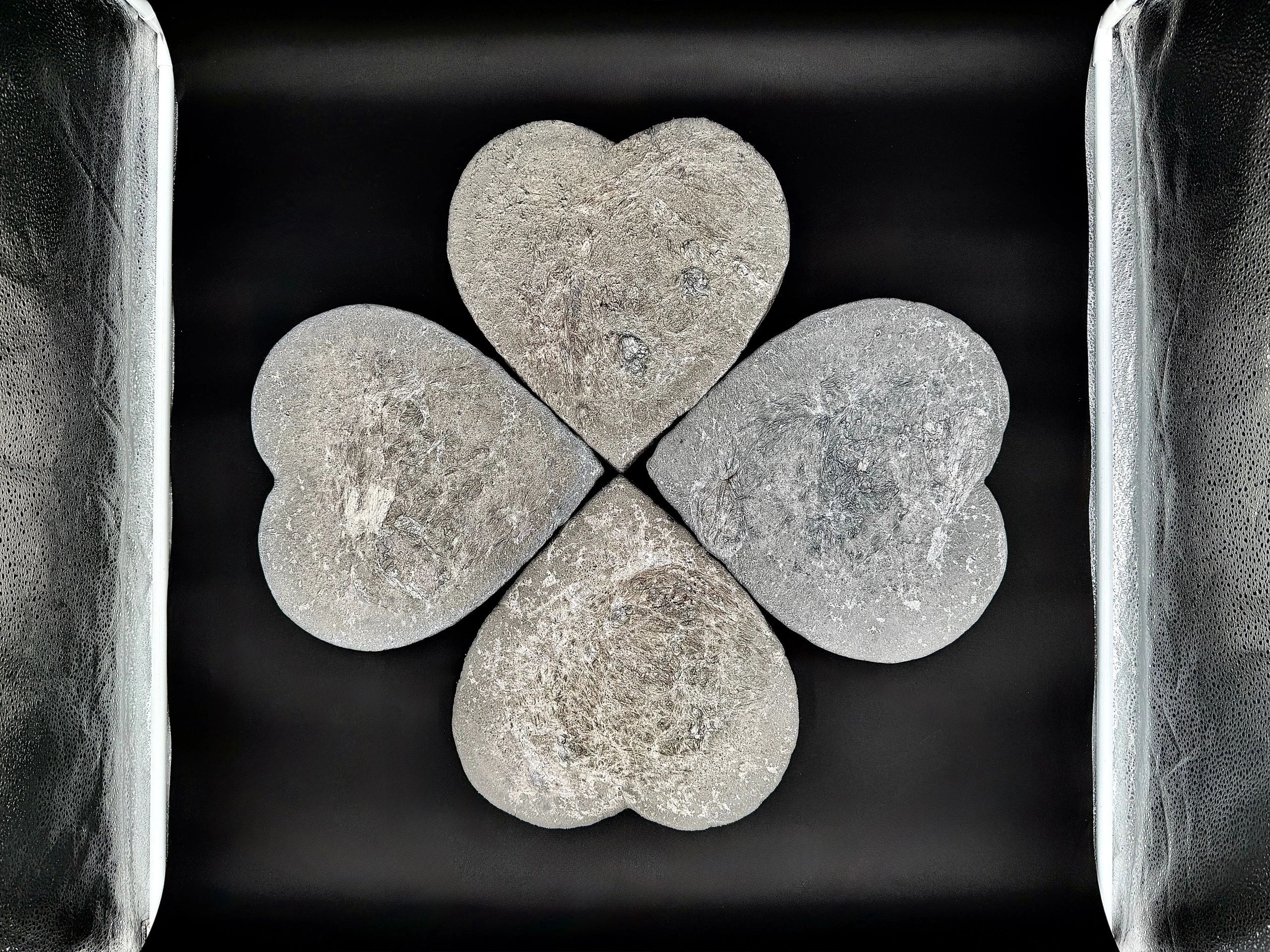 Four heart-shaped stones arranged in a flower pattern on a black surface.