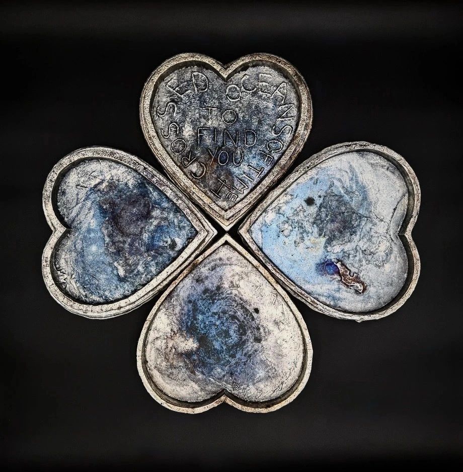 Four heart-shaped metallic objects arranged in a clover pattern on black background.
