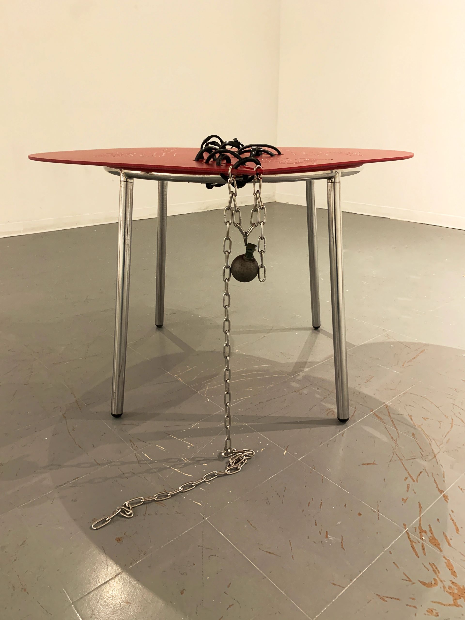 Metal table with a red top and a heavy chain attached.