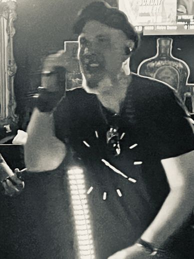 Man in black shirt and cap gesturing indoors with a blurred background.