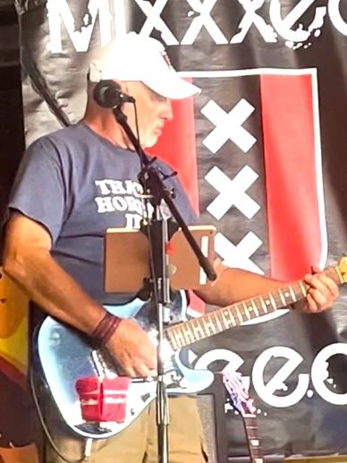 Man playing electric guitar on stage wearing a white cap.