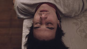 image of young man lying on a table. he faces the camera upside-down with eyes closed