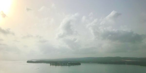 A hazy emerald ocean and silver-blue sky with the edge of a dark green hilly land in the distance.