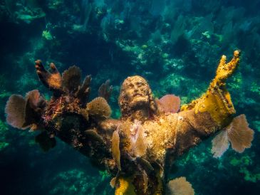 Underwater statue with coral and marine life.