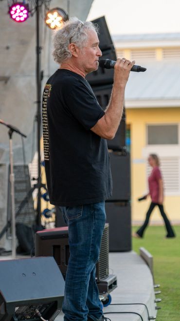 Man speaking into a microphone on an outdoor stage.