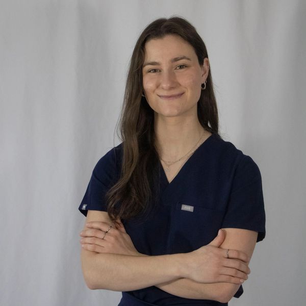 A woman in navy scrubs smiling with arms crossed.