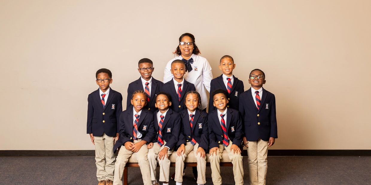 A group of young boys in school uniforms with their teacher, posing for a photo.