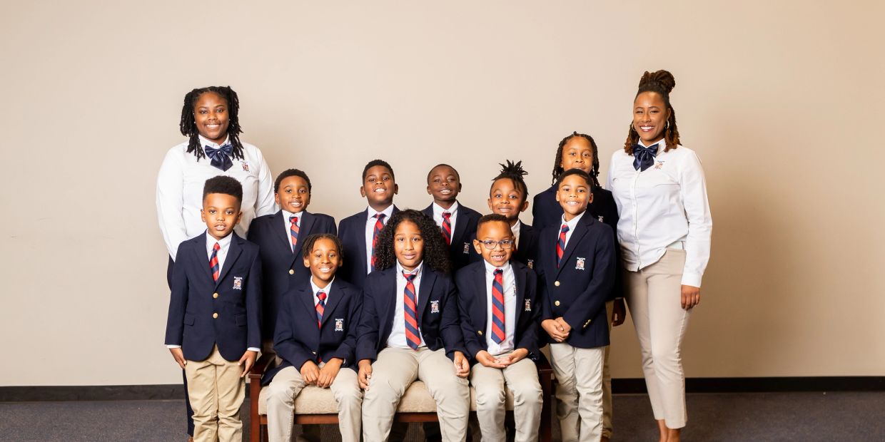 Group of children and two adults in school uniforms posing for a photo.