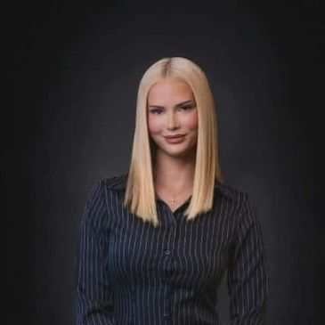 A confident woman with straight blonde hair in a dark striped shirt.