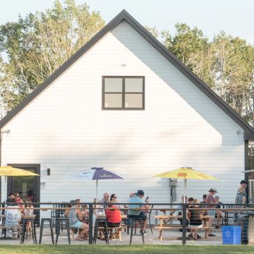 People enjoying outdoor seating at a white building with umbrellas.