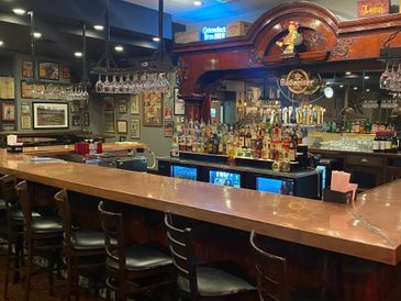 Cozy bar with wooden counter and multiple liquor bottles under warm lighting.