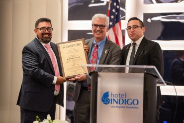 Three men in suits presenting a certificate at Hotel Indigo event.