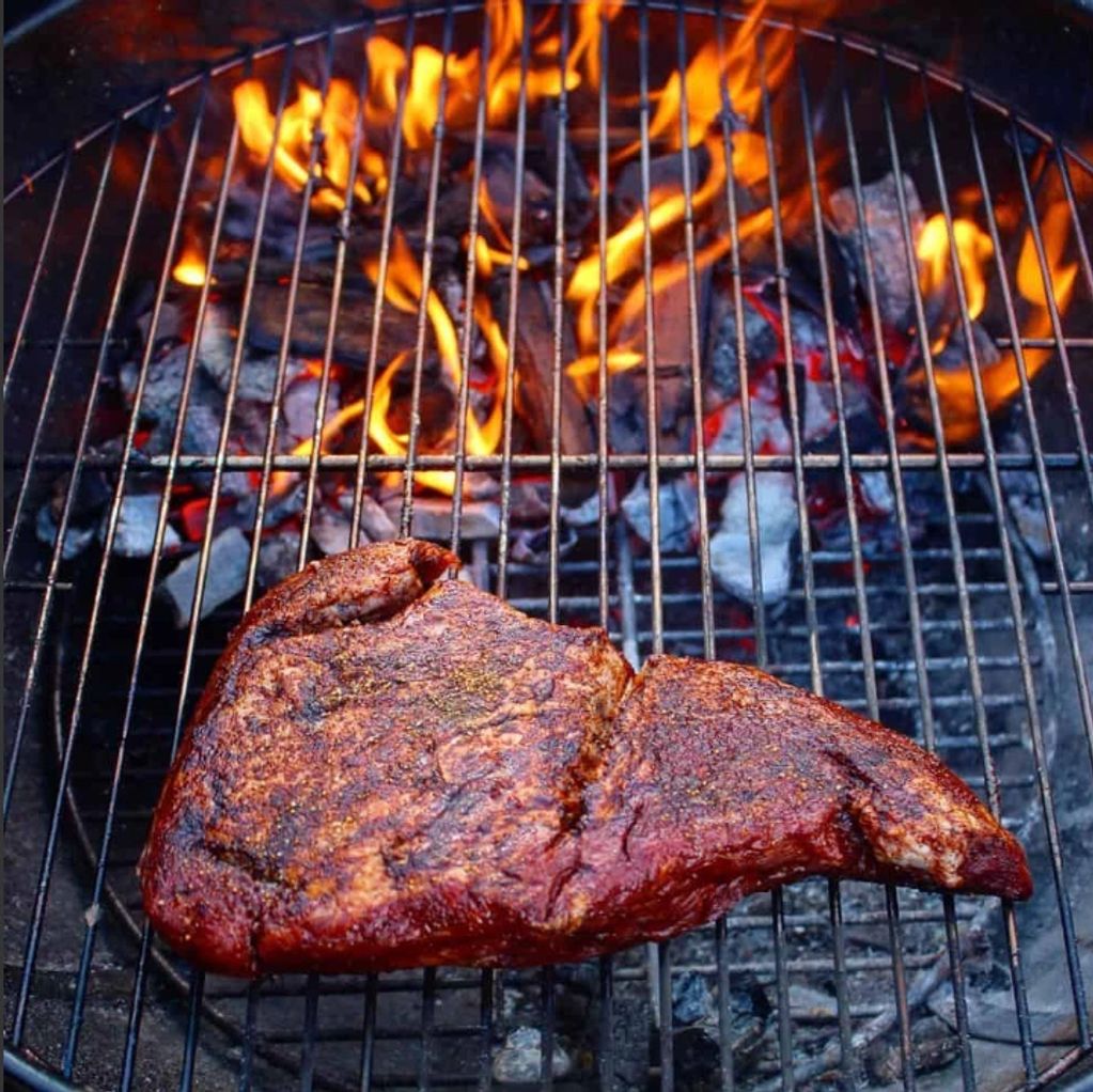Steak grilling on fiery charcoal grill.