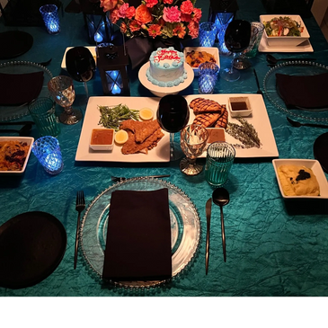 Elegant dinner setup with gourmet dishes and a birthday cake on a teal tablecloth.
