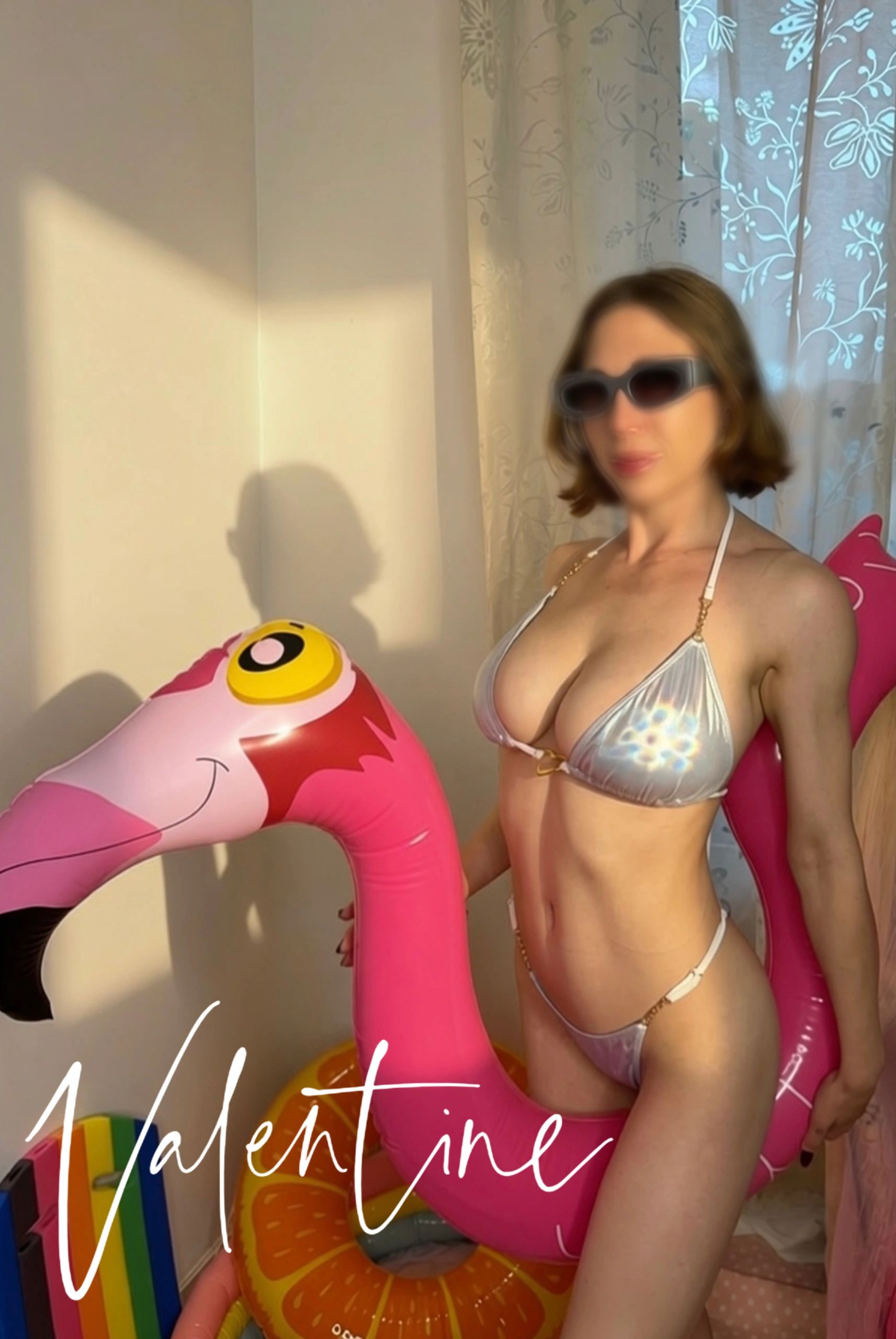 Woman in bikini with inflatable flamingo inside a room.