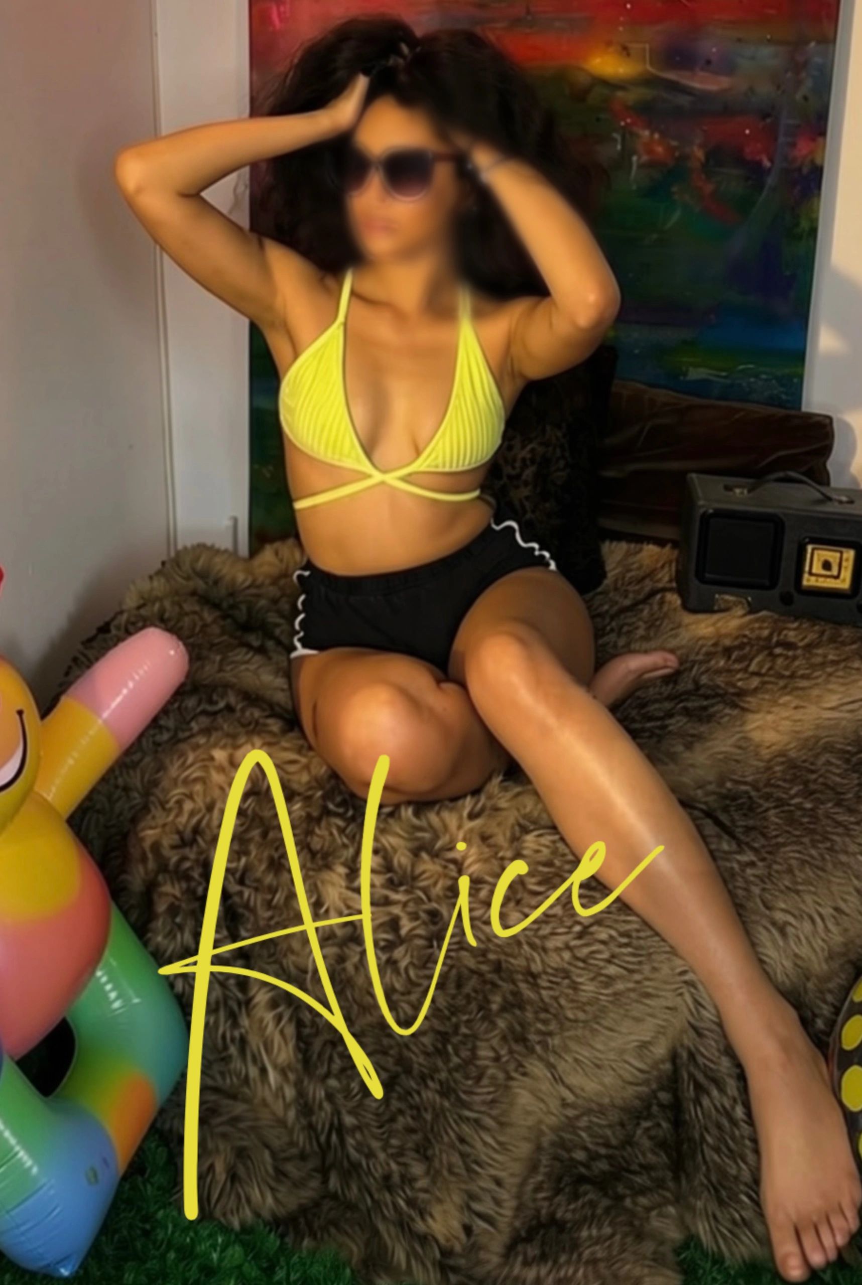 Woman in yellow bikini top and black shorts posing indoors.