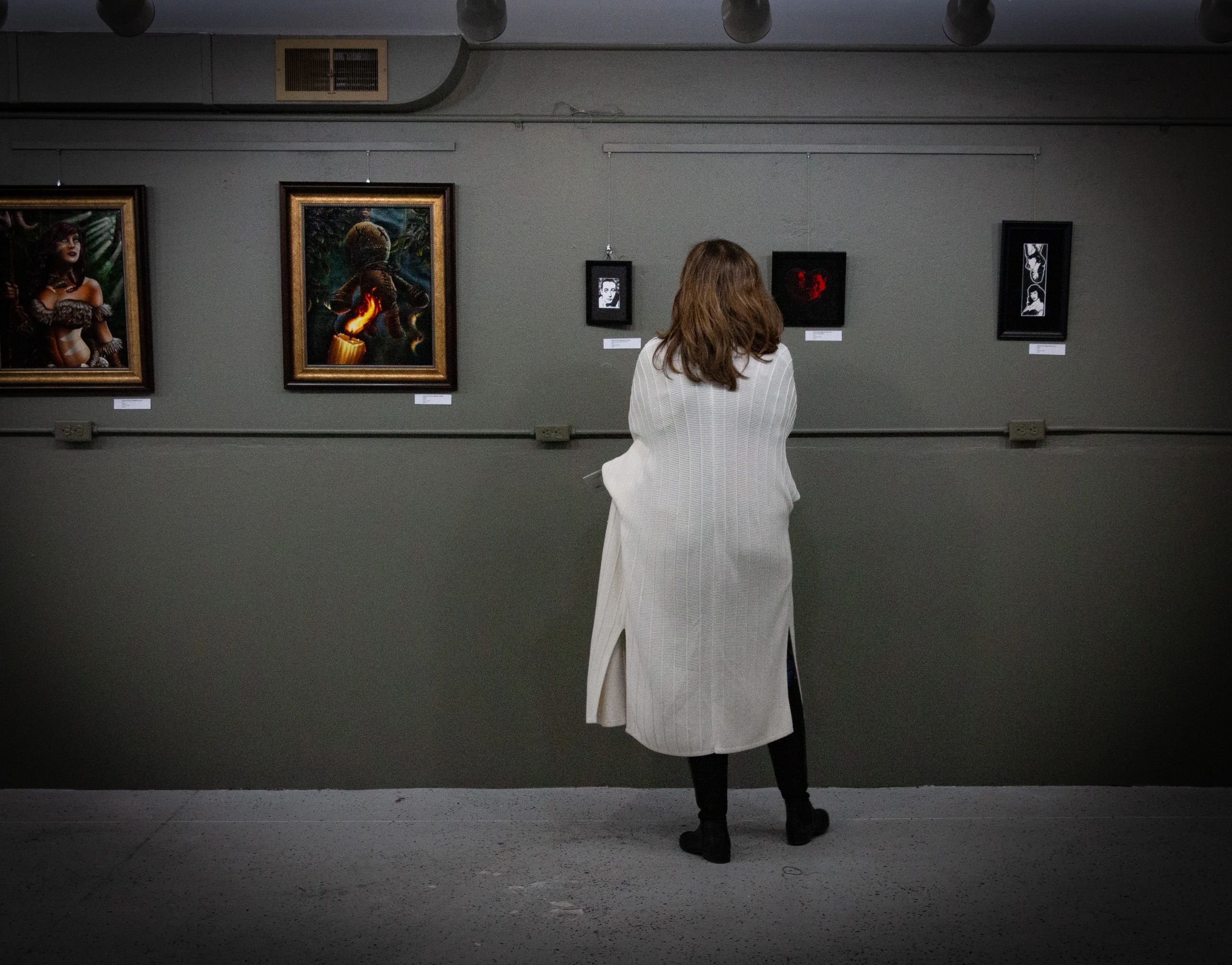 Person viewing framed art in a gallery with dim lighting.