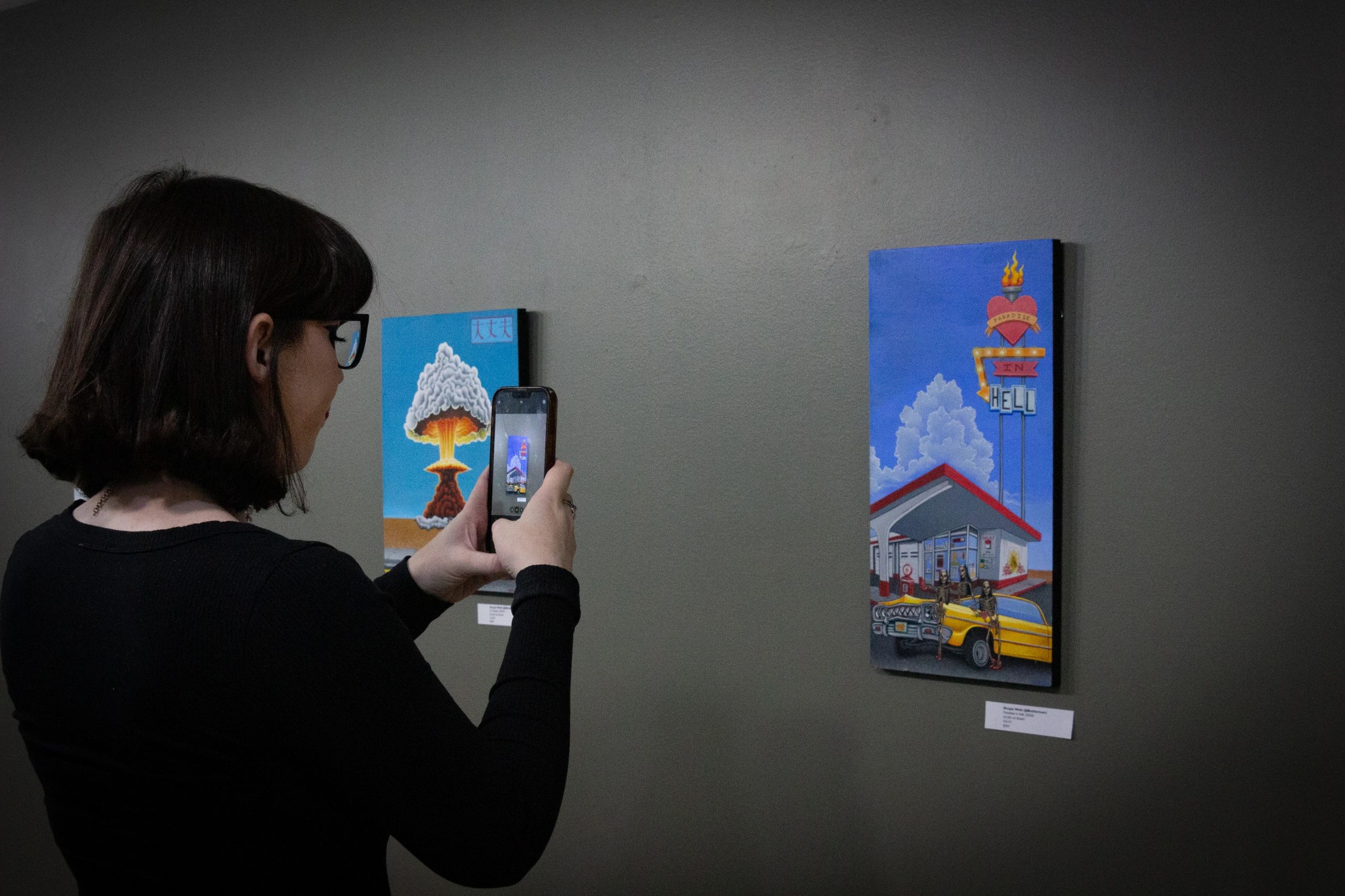 A woman takes a photo of colorful paintings in an art gallery.