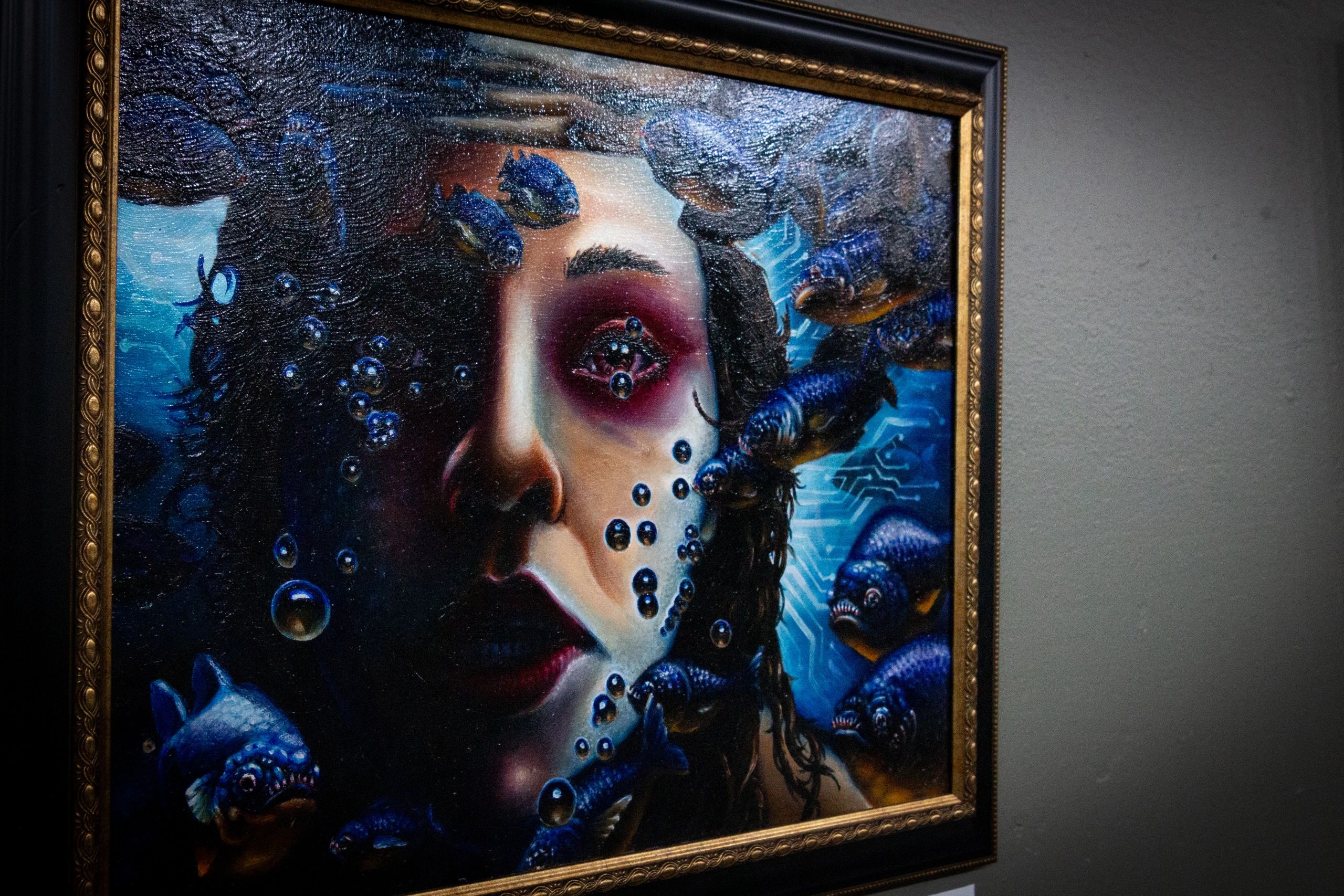 Surreal painting of a woman's face underwater with blue fish and bubbles.