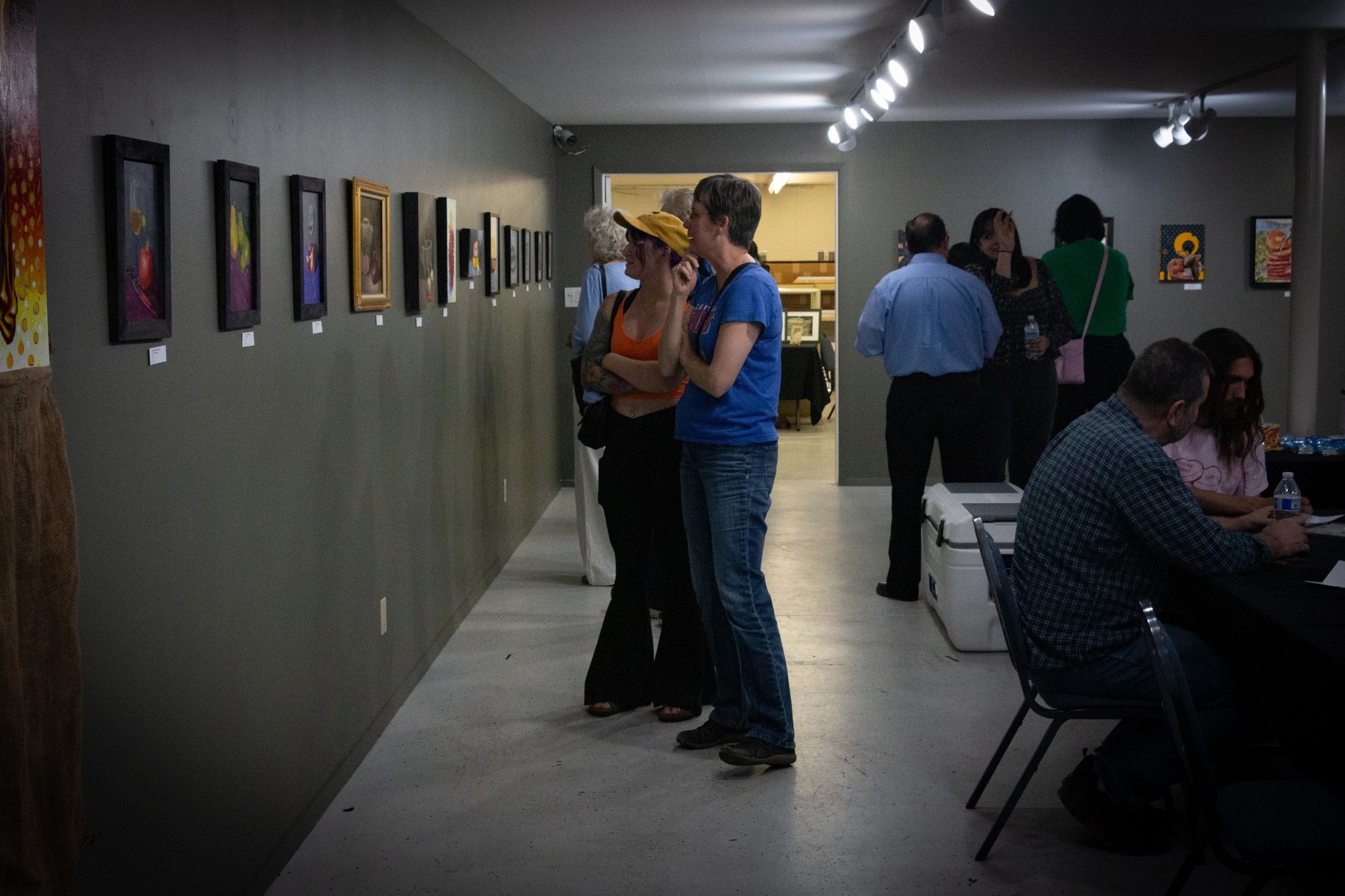People viewing art in a dimly lit gallery with paintings on walls.