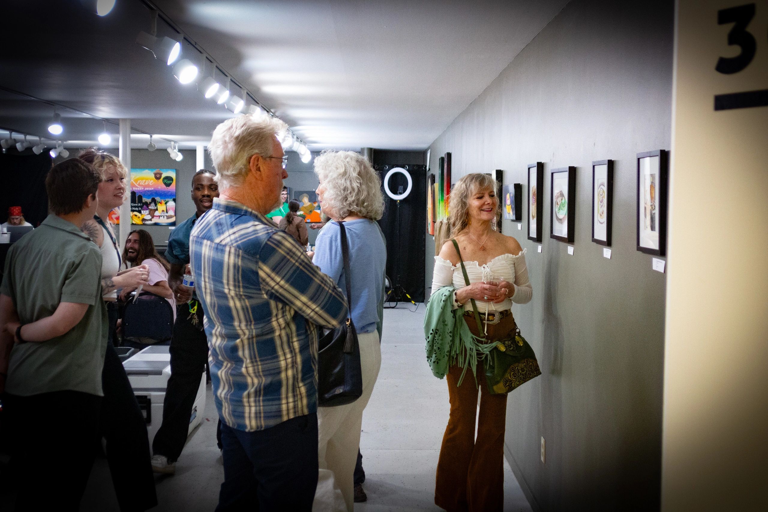 People enjoying art in a gallery with framed paintings on the wall.