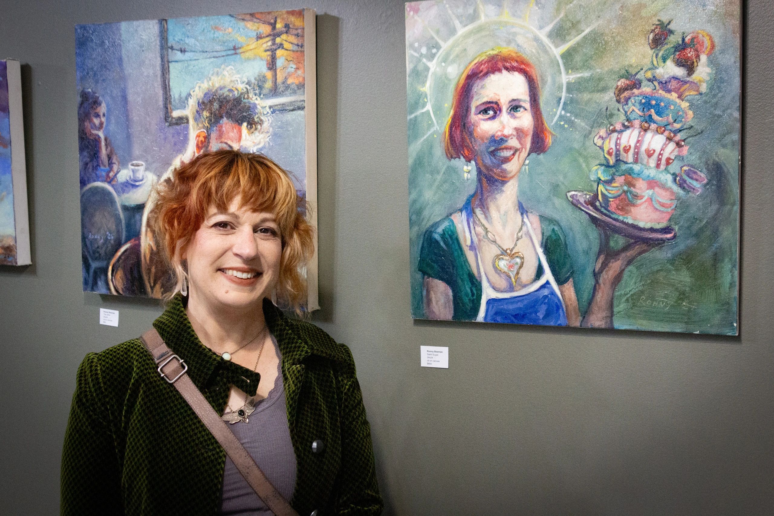 A smiling woman stands in front of colorful paintings at an art gallery.