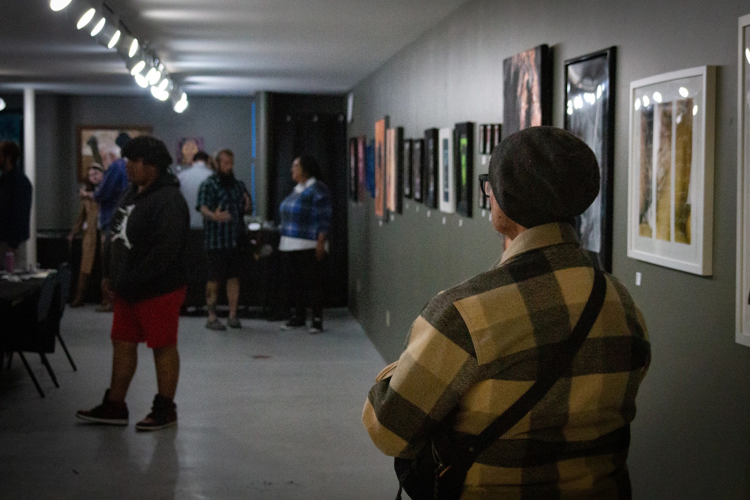 People exploring an art gallery with framed artwork on the walls.