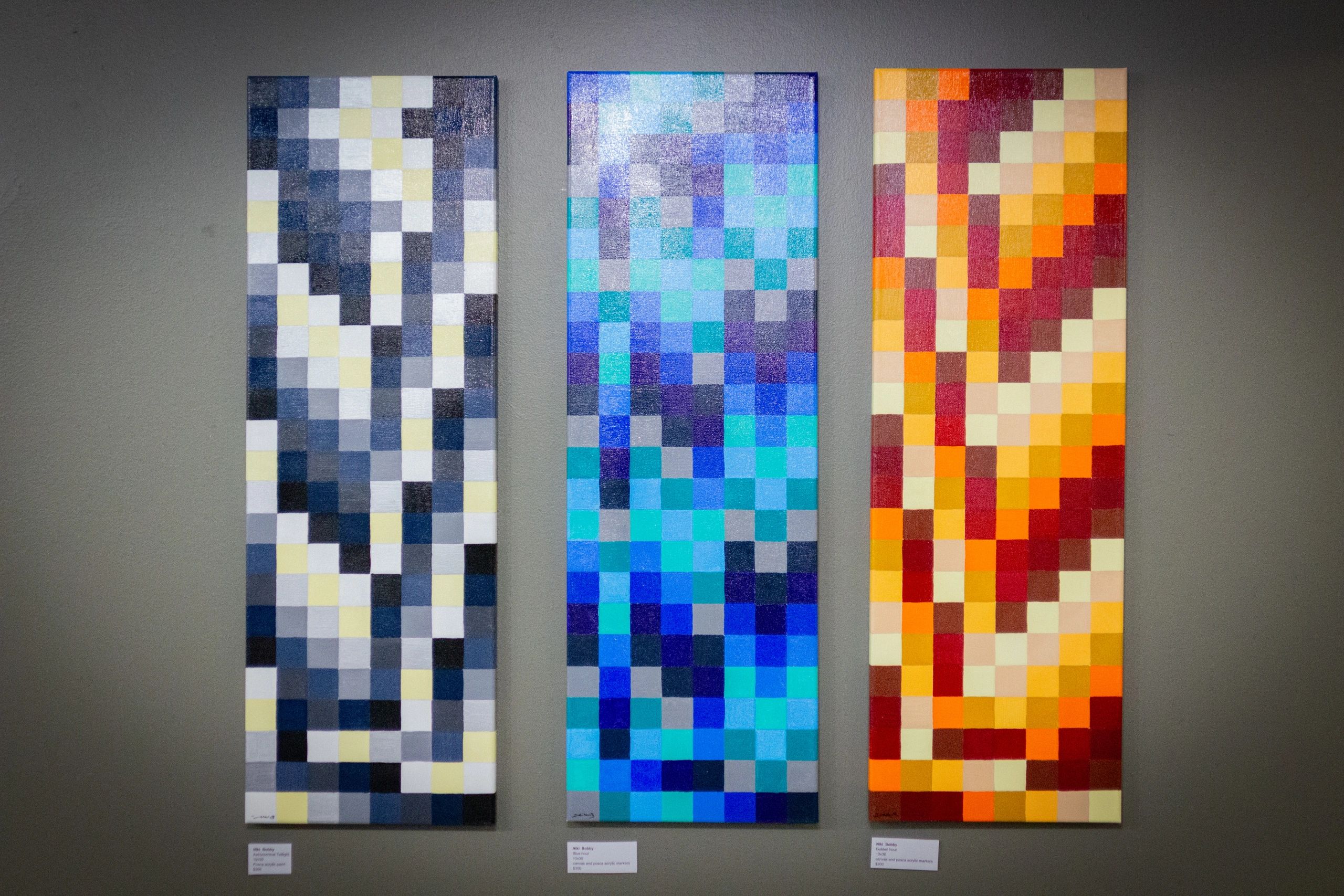 Three vertical abstract pixel art paintings in gray, blue, and warm tones.