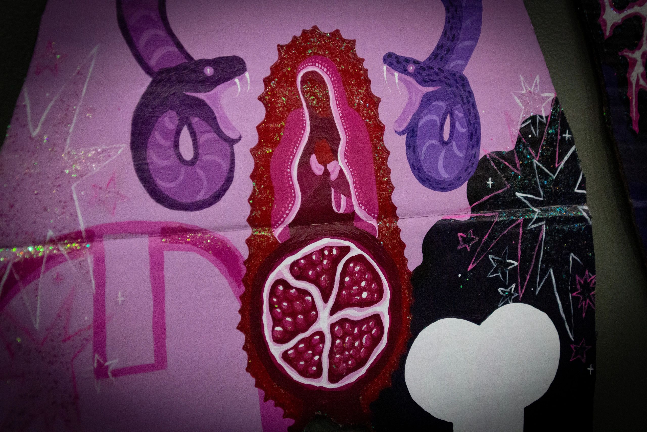 Colorful mural with snakes, pomegranate, and stars on a pink background.