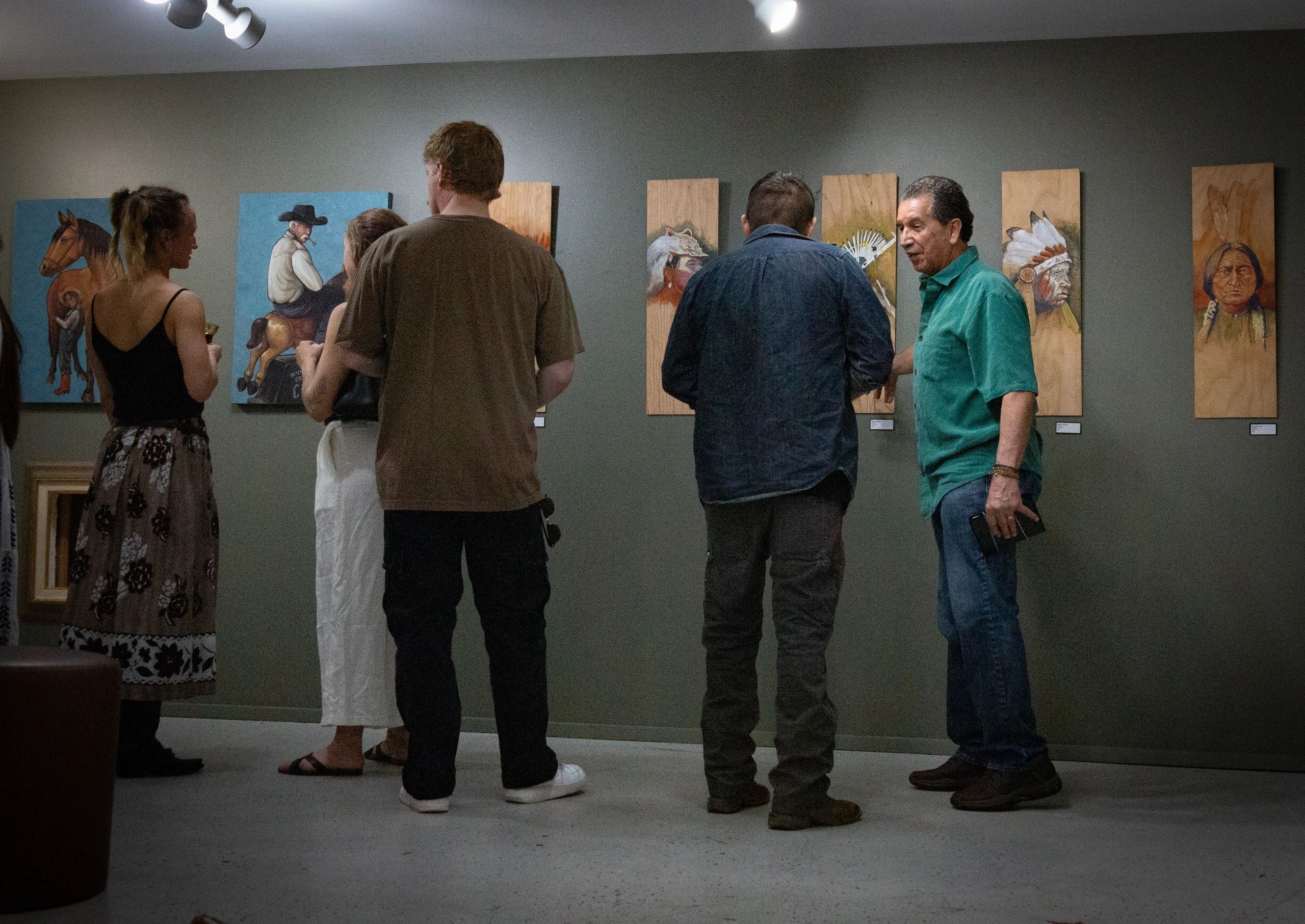 People viewing Native American-themed artwork in a gallery.